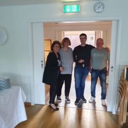 Vier Personen stehen lächelnd unter einem beleuchteten Notausgangsschild neben einem Tisch mit gestapelten Tellern.