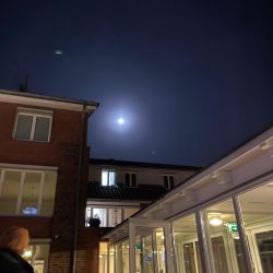 Der helle Mond leuchtet über einem städtischen Gebäude, während eine Person den nächtlichen Anblick draußen genießt.