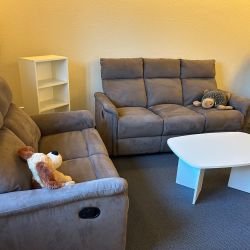 Ein gemütliches Wohnzimmer mit zwei grauen Sofas, einem weißen Couchtisch und Kuscheltieren auf den Sofas.