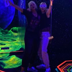 Zwei Personen feiern ausgelassen in einer leuchtenden Schwarzlichtumgebung mit futuristischen Dekorationen.