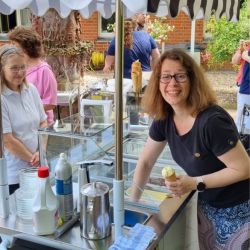 Unter einem gestreiften Sonnenschirm serviert eine Frau lächelnd köstliches Eis an einem belebten Eisstand.