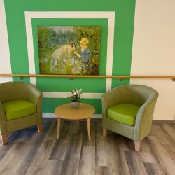 Zwei grüne Sessel und ein Tisch mit Blumen stehen vor einer grünen Wand mit einem impressionistischen Gemälde.