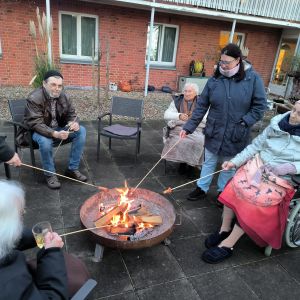 Menschen sitzen um eine Feuerstelle und rösten Würstchen, um eine gemütliche Zeit im Freien zu genießen.