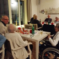 Ältere Menschen sitzen in einem gemütlichen Raum an festlich dekorierten Tischen und genießen eine gesellige Runde.