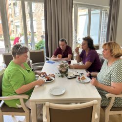 Vier Frauen sitzen an einem Tisch und genießen Kuchen in einem lichtdurchfluteten Raum bei einem entspannten Treffen.