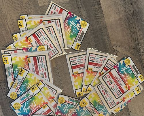 Mehrere bunte 25-Euro-Gutscheine liegen zur Mitarbeiteranerkennung ordentlich auf einem Holzboden bereit.