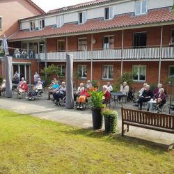 Senioren genießen die sonnige Atmosphäre im Garten eines Wohnheims und entspannen sich zusammen im Freien.