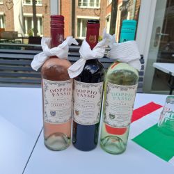 Drei Doppio Passo Weinflaschen stehen neben einem umgedrehten Glas auf einem Tisch mit einer italienischen Flagge.