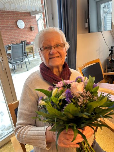 Eine lächelnde ältere Dame hält einen bunten Blumenstrauß im Wohnzimmer.