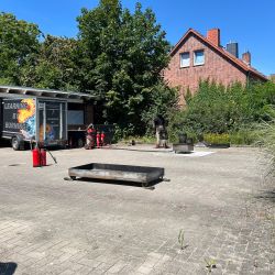 Ein Übungsplatz mit Feuerlöschausrüstung und einem Anhänger mit "Learning by Burning" bei strahlendem Sonnenschein.
