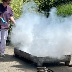 Eine Person führt im Freien eine Brandschutzübung durch, indem sie mit einem Feuerlöscher dichten Rauch erzeugt.