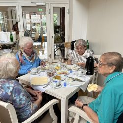 Vier ältere Personen sitzen in einem Café, genießen eine Mahlzeit und führen eine lebhafte Unterhaltung bei Kaffee.