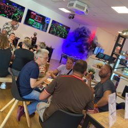 Menschen genießen entspannte Unterhaltung an Tischen in einem lebhaften Raum mit bunten Arcade-Spielen.