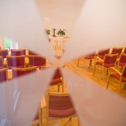 Ein heller Kirchenraum mit roten Stühlen und einem Altar wird durch eine sternförmige Glasscheibe betrachtet.