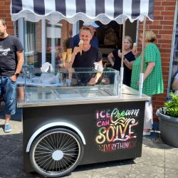 Ein Mann verkauft Eiscreme an einem schwarz-weiß gestreiften Stand mit dem Slogan "Ice Cream Can Solve Everything".