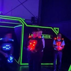 Personen spielen Lasertag in einer dunklen Arena mit leuchtenden Westen und Waffen, die in lebhaften Farben aufleuchten.