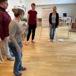 Eine Gruppe von fünf Personen steht in einem hellen Raum um ein Flipchart und nimmt an einem Workshop teil.