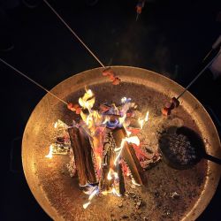Würstchen werden auf langen Stöcken über einem lebhaften Feuer gegrillt, während die Flammen hoch lodern.