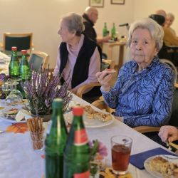 Ältere Damen genießen Kuchen und Getränke in einem festlich dekorierten Raum mit herbstlichen Blumenarrangements.