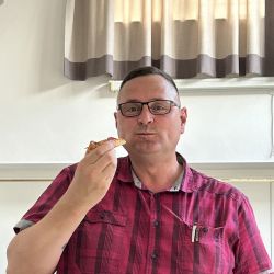 Ein Mann in einem roten karierten Hemd genießt ein Stück Pizza in einem hell erleuchteten Raum.