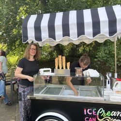 Eine Frau lächelt neben einem Eiswagen im Freien, während eine Person köstliches Eis serviert.