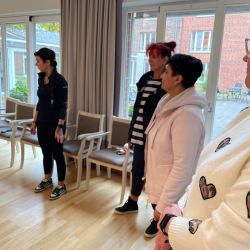 Mehrere Menschen stehen in einem hellen Raum mit Holzboden und unterhalten sich entspannt.