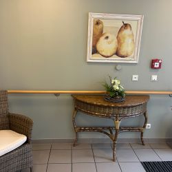 Ein gemütlicher Flur zeigt einen geflochtenen Stuhl, einen Tisch mit Blumendekoration und ein Birnenbild an der Wand.