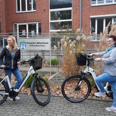 Zwei Frauen unterhalten sich lebhaft über ihre Jobrad-Erfahrungen vor dem Posener Altenheim mit ihren E-Bikes.