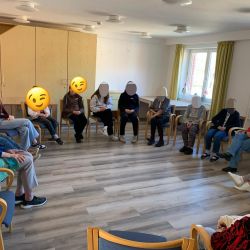 Eine Gruppe von Menschen sitzt in einem hellen Raum im Kreis und führt eine lebhafte Gesprächsrunde durch.