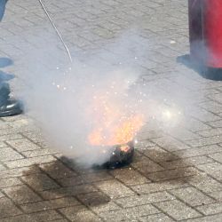 Ein Feuerlöscher wird eingesetzt, um ein kleines Feuer auf dem Boden zu löschen, während Funken und Rauch aufsteigen.
