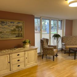 Ein gemütliches Wohnzimmer mit beigen Sesseln, einem Sofa und einer braunen Kommode unter einem Landschaftsgemälde.