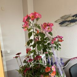 Ein großer, bunter Blumenstrauß steht in einem geflochtenen Korb neben einer Wand mit Fischdekoration.