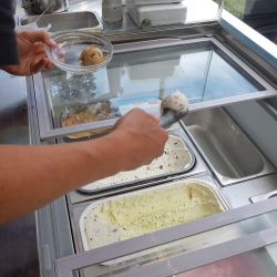 In einem gemütlichen Café schöpft eine Person zwei Eiskugeln aus der Eistheke in eine Schale.