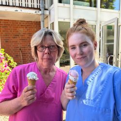 Zwei Personen in bunter Arbeitskleidung genießen Eis vor einem Gebäude mit Glasfassade.
