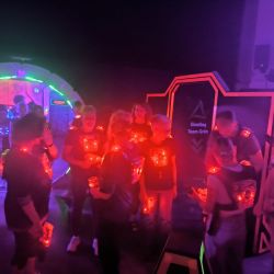 Eine Gruppe von Menschen bereitet sich in einer bunten Laser-Tag-Arena auf das Spiel vor, beleuchtet von roten Lichtern.