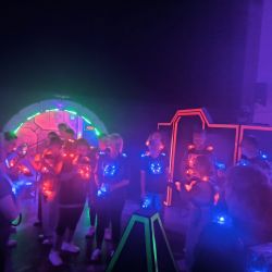 Eine Gruppe von Menschen spielt Lasertag mit leuchtenden Westen in einem dunklen Raum voller bunter Lichter.