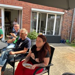 Eine Gruppe von Menschen sitzt im Garten, isst Pizza und genießt das sonnige Wetter.