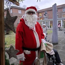 Ein Weihnachtsmann in rotem Kostüm verteilt Geschenke an die Bewohner vor einem Pflegeheim im Freien.