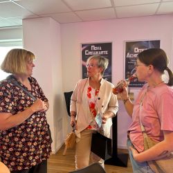 Drei Frauen unterhalten sich lebhaft in einem Raum, während eine ein Getränk in der Hand hält.