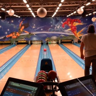 Zwei Personen spielen Bowling in einer bunt bemalten Halle mit Comicfiguren, die eine dynamische Atmosphäre schafft.