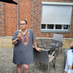 Drei Frauen genießen Eis und unterhalten sich entspannt auf einer Terrasse vor einer Ziegelwand.