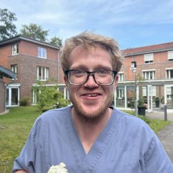 Ein Mann in blauer Kleidung genießt ein Eis vor einem Backsteingebäude im Freien an einem sonnigen Tag.