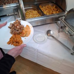 Eine Person füllt ihren Teller mit Reis, Fleisch und Pommes von einem warmen Buffet.