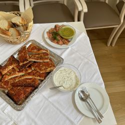 Ein gedeckter Tisch bietet Pizzastücke, Brot, Lachs und Dips auf weißen Tischdecken zum Genießen an.