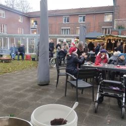 Menschen feiern im Innenhof eines Pflegeheims mit Weihnachtsdekoration und sitzen gemütlich an festlich gedeckten Tischen zusammen.