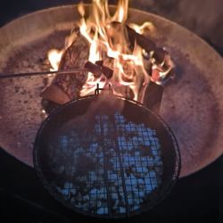 Marshmallows werden über einem offenen Feuer geröstet, während ein Grillkorb mit weiteren Marshmallows bereitsteht.