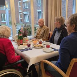 Eine Gruppe älterer Menschen sitzt lebhaft plaudernd um einen gedeckten Tisch in einem gemütlichen Raum.