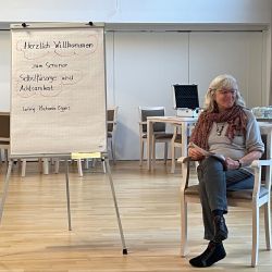 Eine Frau sitzt neben einem Flipchart, das ein Seminar zu Selbstfürsorge und Achtsamkeit ankündigt.