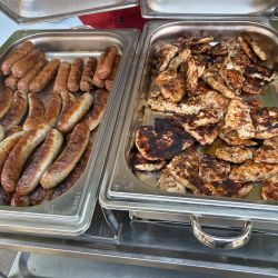Gegrillte Würstchen und Fleisch liegen in zwei silbernen Schalen auf einem Buffet bereit und laden zum Genießen ein.