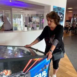Eine Frau spielt konzentriert an einem Star Wars-Flipperautomaten in einem modernen Raum mit futuristischer Dekoration.